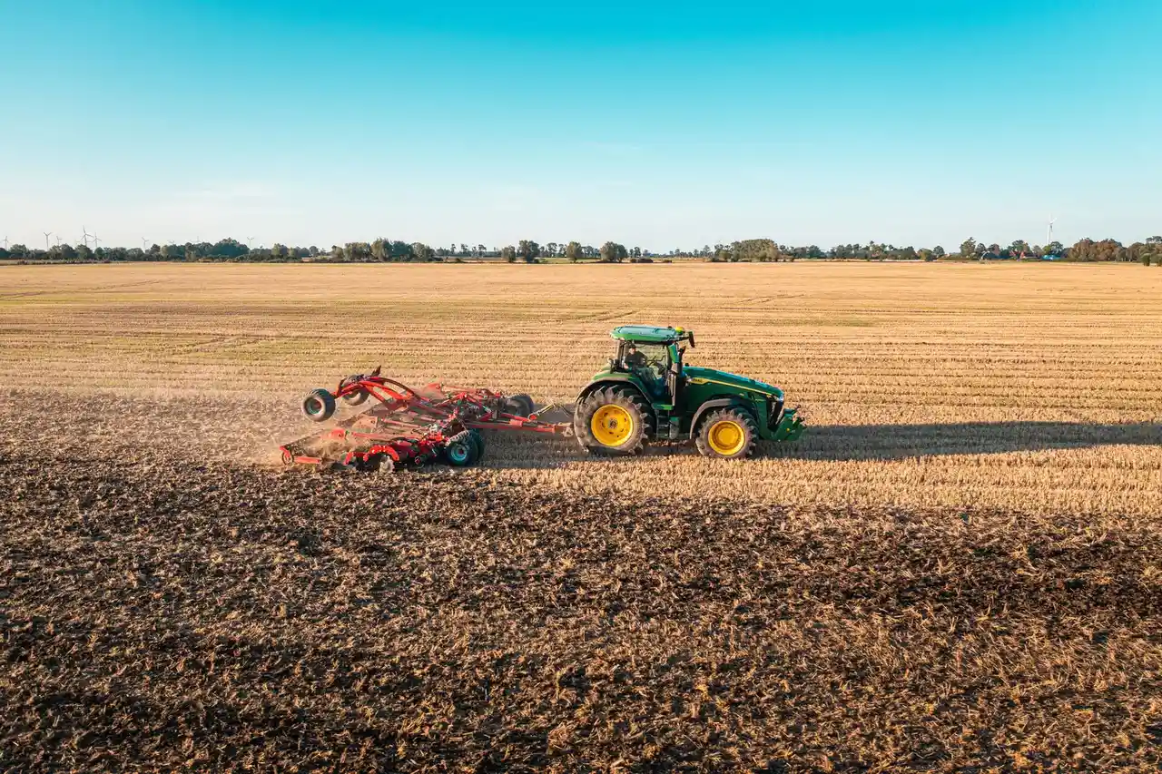 Ciągnik John Deere z agregatem Ciągnik John Deere ciągnie agregat uprawowy po polu.